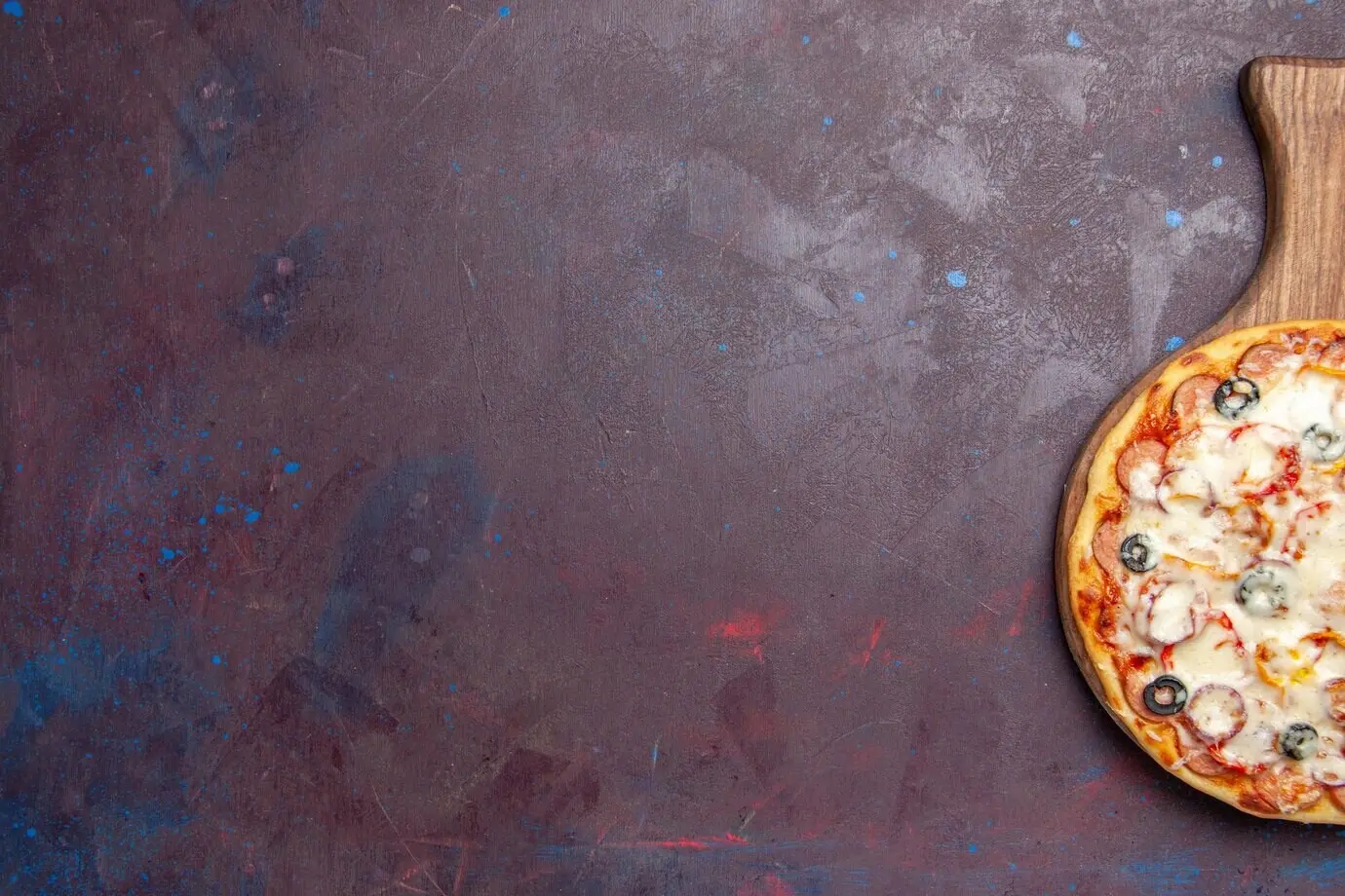 Top view of a delicious mushroom pizza with cheese, olives, and tomatoes on a dark floor; an Italian meal, dough, pizza food.