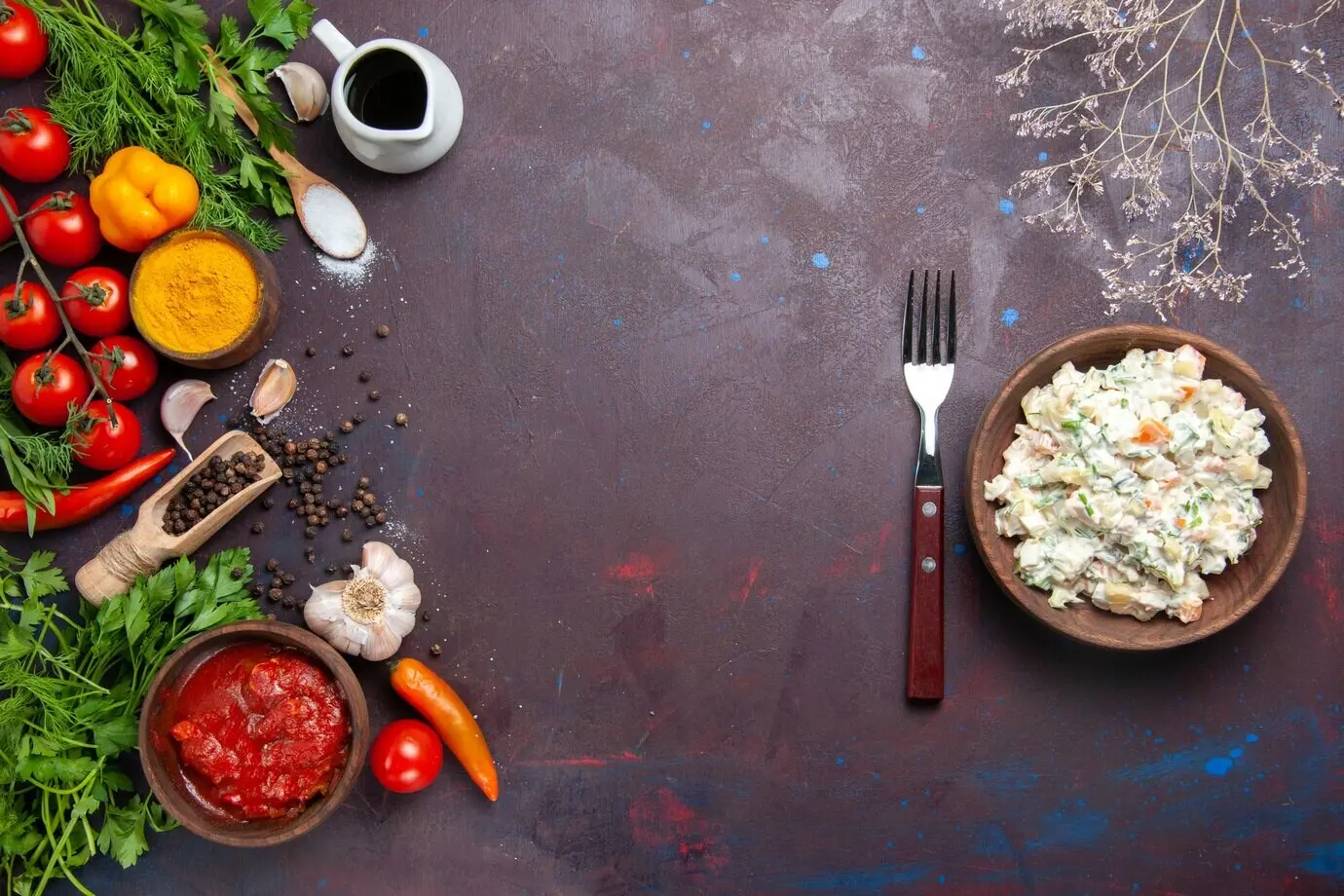 Overhead view of a mayonnaise salad with greens and vegetables on a dark desk.