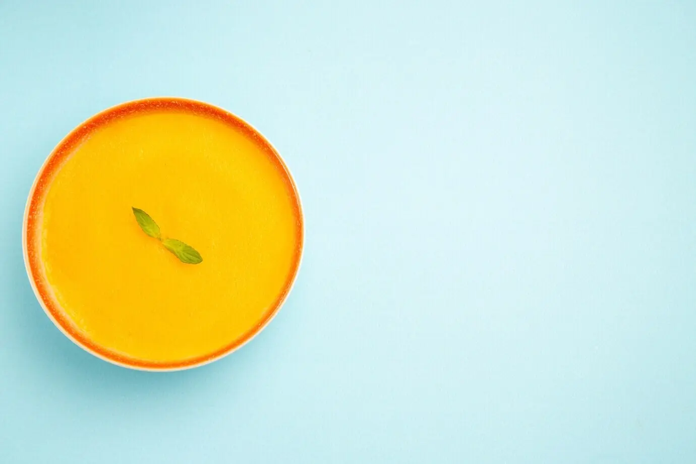 Overhead view of pumpkin soup in a plate on a blue desk